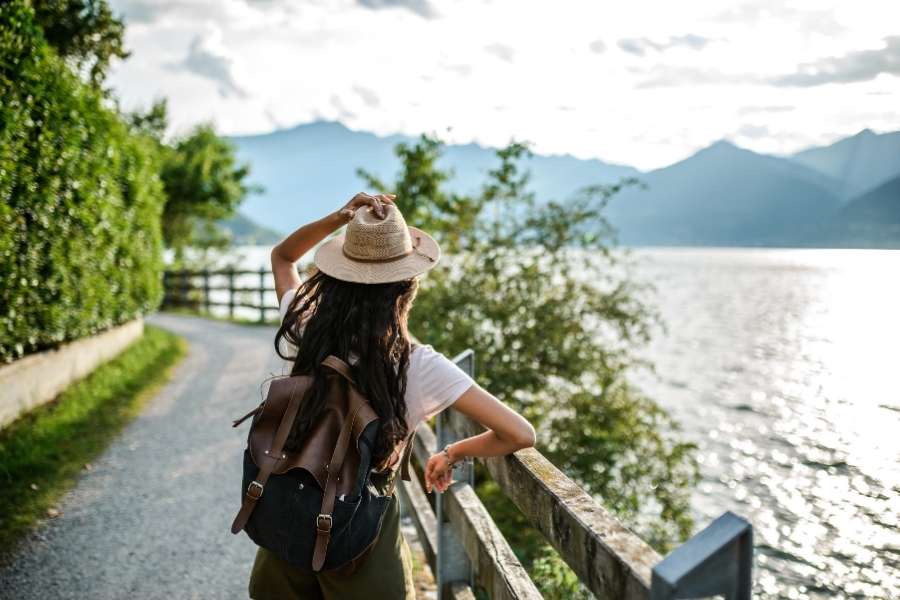 Une jeune femme avec un chapeau de paille et un sac à dos admire un lac alpin entouré de montagnes en voyageant en Europe.