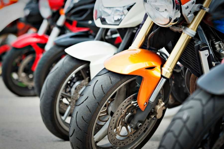 Plusieurs motos aux équipements moto modernes alignées, avec des roues avant, fourches et carénages colorés en orange, blanc et rouge bien visibles.