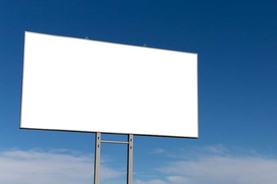 Un grand panneau d'affichage blanc et vierge se détache sur un ciel bleu, idéal pour simuler le rendu d'une oriflamme personnalisée.