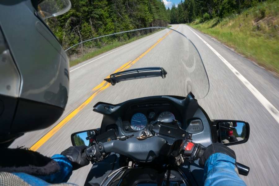 Un motard conduit sur une route sinueuse en forêt en regardant à travers son pare-brise moto.