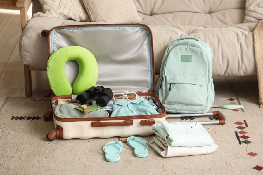 Une valise ouverte et un sac à dos préparés avec soin, illustrant l'art de voyager léger avec des accessoires essentiels.