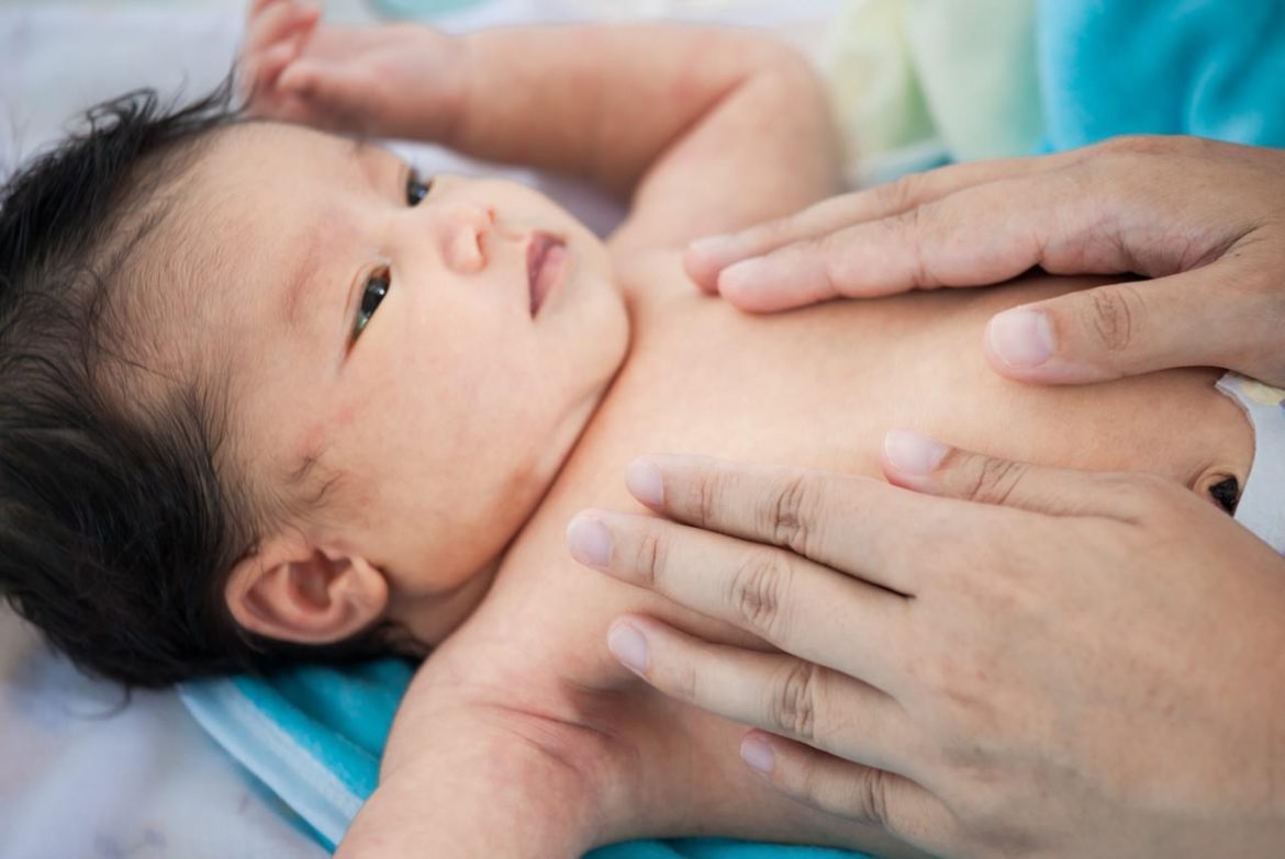Mains d'un parent effectuant un massage bébé pour apaiser les coliques et le sommeil de son nouveau-né allongé sur une serviette bleue.