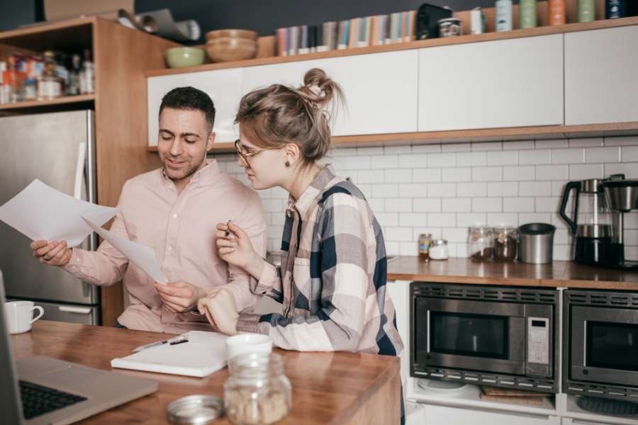Un couple analyse ses documents financiers dans la cuisine pour apprendre à réduire sa facture d'eau.